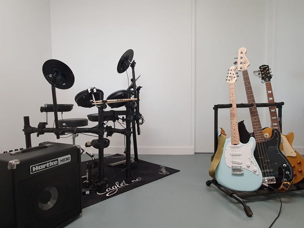 Photographie du studio de musique avec une batterie et trois guitares électriques