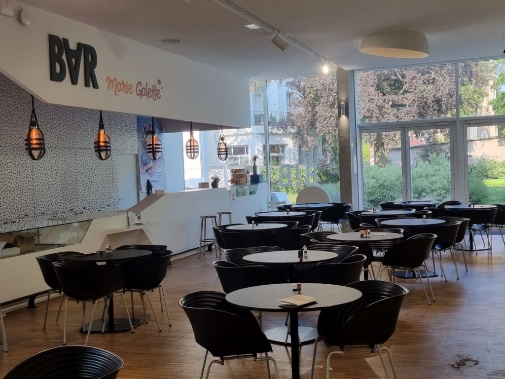 Photo de la cafétéria, ses tables avec chaises et le comptoir dans le hall de la Bib