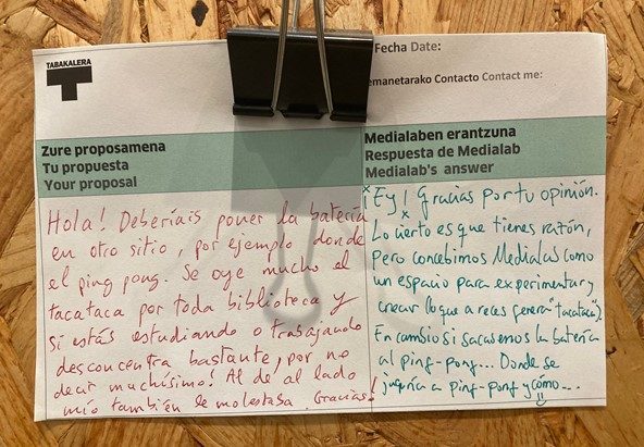 Photo d'un échange écrit entre un usager et la bibliothèque à propos du bruit dû à la pratique musicale dans le studio 
≪ Bonjour ! Vous devriez mettre la batterie ailleurs, par exemple là où se trouve la table de ping-pong. On entend beaucoup le tac tac tac dans toute la bibliothèque et si tu es train d’étudier ou de travailler ça déconcentre pas mal, pour ne pas dire beaucoup ! Autour de moi ça les dérangeait aussi.  
- Salut ! Merci pour ton opinion. Ce qui est certain c’est que tu as raison, mais nous concevons Medialab comme un espace pour expérimenter et créer (ce qui génère parfois des “tac tac tac”). Inversement si on déplace la batterie à la place du ping-pong, où est-ce qu’on jouera au ping-pong, et comment… 🙂 ≫
© Bpi