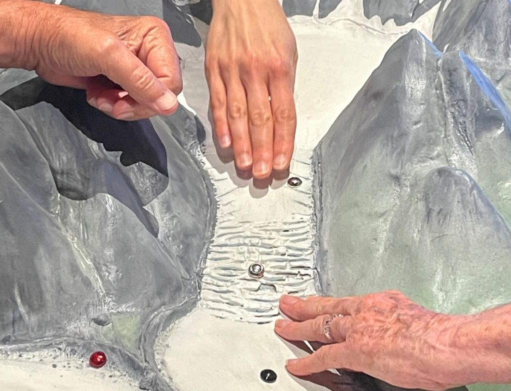 Des mains touchent un pan d'exposition en relief.