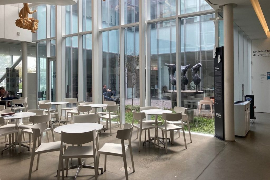 Café à l'intérieur de la bibliothèque, très lumineux, devant une grande baie vitrée, avec des sculpures suspendues au plafond.