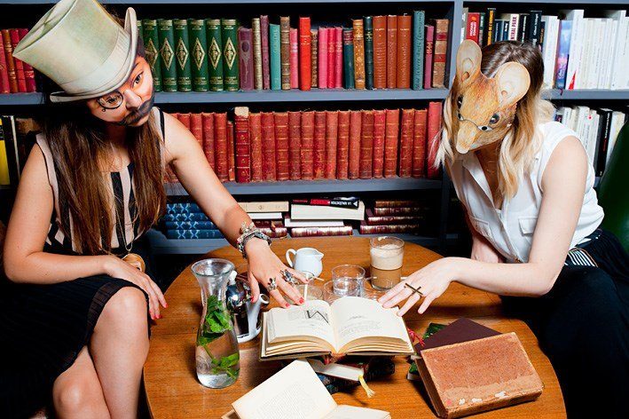 Photographie de deux femmes masquées lisant le même livre devant une bibliothèque