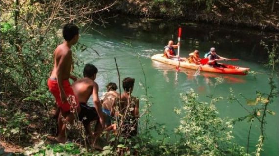 Image du documentaire avec un groupe d'enfants sur la rive d'un ruisseau sur lequel passe trois personnes en kayak